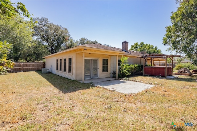 rear view of house with central air condition unit, a gazebo, a patio area, a hot tub, and a lawn