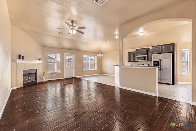 unfurnished living room with dark wood-type flooring, a tiled fireplace, a textured ceiling, and ceiling fan with notable chandelier