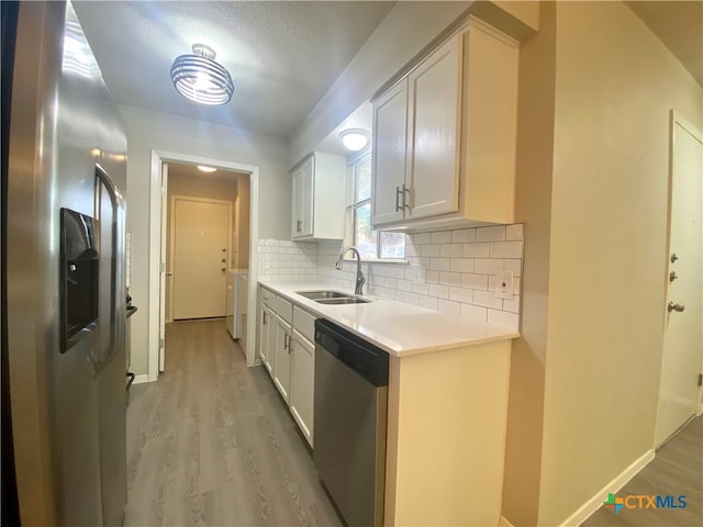 kitchen featuring tasteful backsplash, stainless steel appliances, white cabinetry, sink, and light hardwood / wood-style flooring