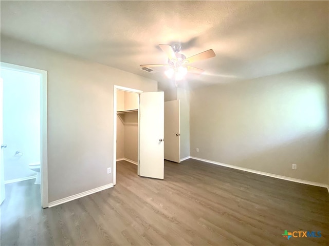 unfurnished bedroom featuring a closet, a spacious closet, wood-type flooring, ceiling fan, and ensuite bathroom