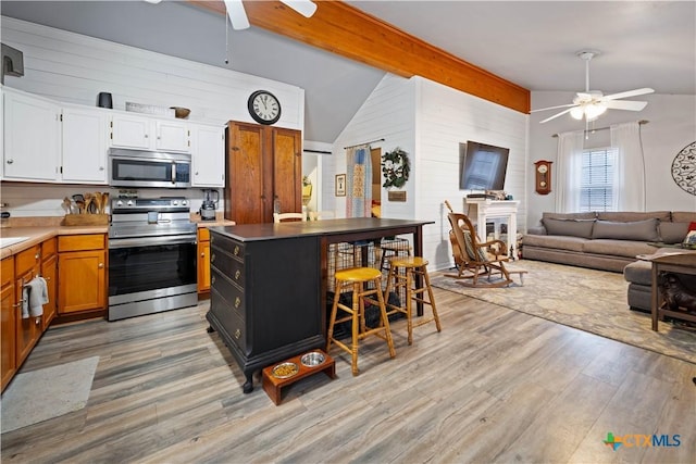 kitchen featuring a breakfast bar, white cabinetry, open floor plan, appliances with stainless steel finishes, and brown cabinets