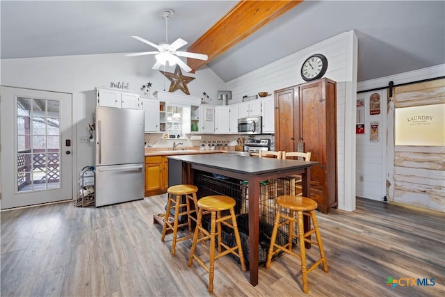 kitchen with a barn door, lofted ceiling with beams, light wood-style flooring, appliances with stainless steel finishes, and white cabinetry