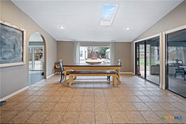 dining space with lofted ceiling, light tile patterned flooring, arched walkways, and baseboards