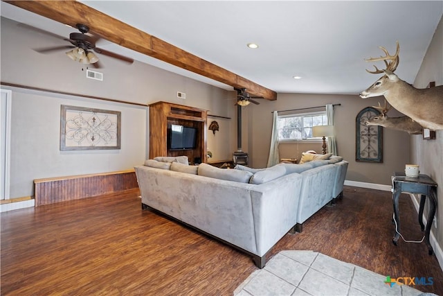 living room with vaulted ceiling with beams, visible vents, a wood stove, wood finished floors, and baseboards