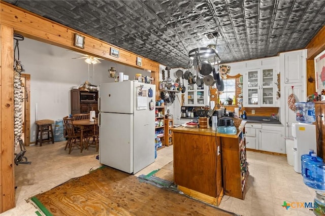 kitchen with an ornate ceiling, freestanding refrigerator, ceiling fan, white cabinetry, and glass insert cabinets