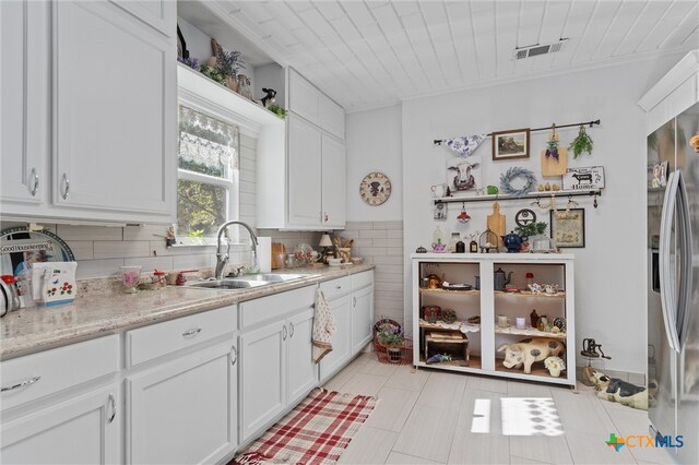 kitchen featuring white cabinets, decorative backsplash, stainless steel refrigerator with ice dispenser, sink, and light stone countertops