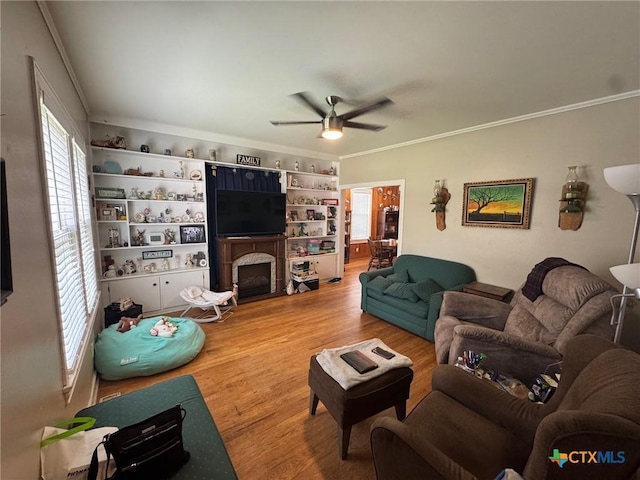 living room featuring a ceiling fan, a healthy amount of sunlight, crown molding, and wood finished floors