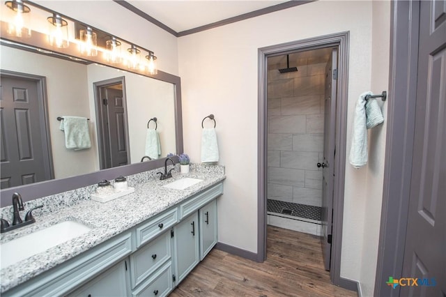 bathroom featuring vanity, wood-type flooring, tiled shower, and ornamental molding