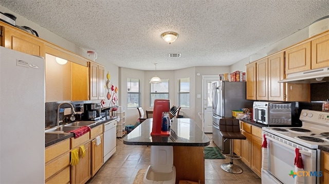 kitchen featuring dark countertops, a sink, white appliances, under cabinet range hood, and visible vents