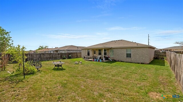 rear view of house with a lawn, a fire pit, a fenced backyard, a patio, and brick siding