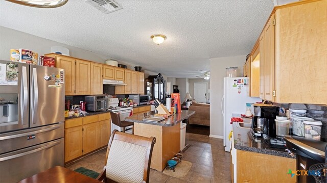 kitchen with visible vents, a ceiling fan, a center island, a textured ceiling, and appliances with stainless steel finishes