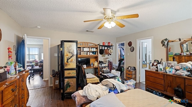 bedroom featuring a textured ceiling, dark wood-style flooring, visible vents, a spacious closet, and a ceiling fan