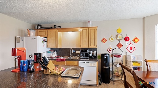 kitchen featuring dark countertops, light brown cabinets, a sink, white appliances, and a textured ceiling