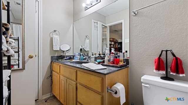 full bathroom featuring tile patterned floors, vanity, a textured wall, toilet, and visible vents
