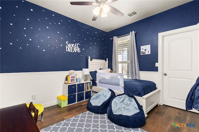 bedroom featuring ceiling fan, wood finished floors, visible vents, and wainscoting