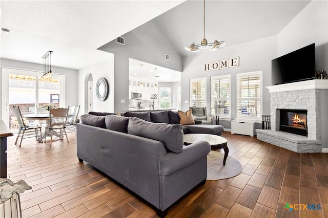 living area featuring a stone fireplace, high vaulted ceiling, visible vents, and wood tiled floor