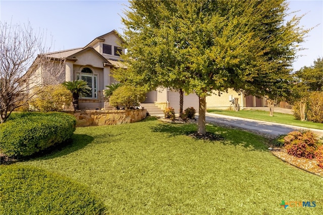 view of property hidden behind natural elements with stucco siding, driveway, and a front lawn