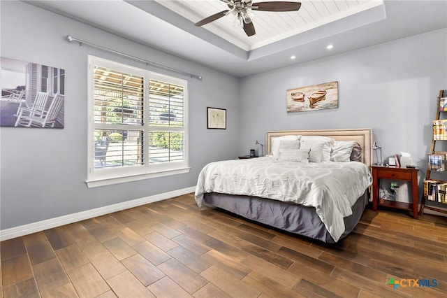 bedroom with recessed lighting, a tray ceiling, baseboards, and wood finished floors