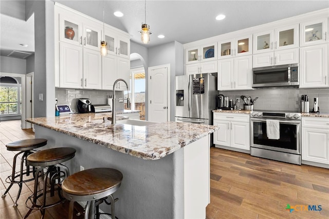 kitchen with wood finished floors, a breakfast bar, arched walkways, a sink, and appliances with stainless steel finishes