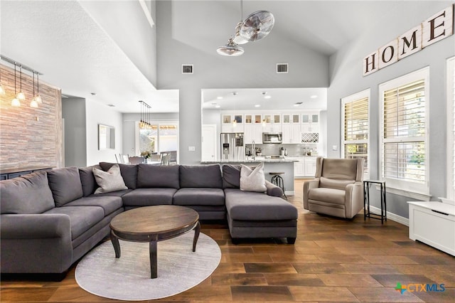 living room with visible vents, baseboards, dark wood-type flooring, and a towering ceiling