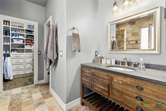 bathroom featuring a walk in closet, baseboards, tiled shower, and vanity