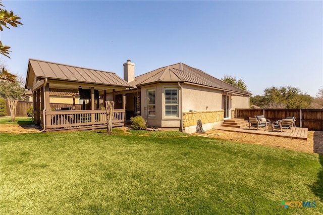 back of property with a wooden deck, a lawn, a standing seam roof, and fence