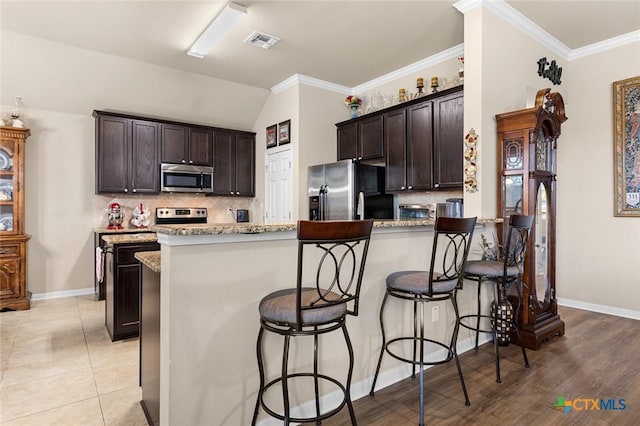 kitchen with backsplash, dark brown cabinetry, light stone countertops, and appliances with stainless steel finishes