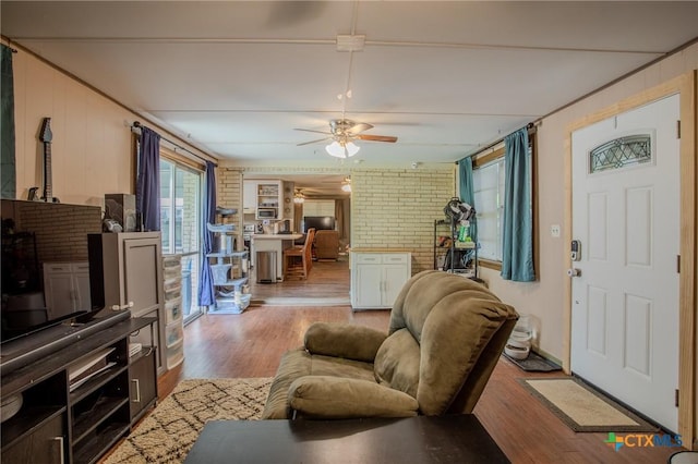 living area featuring a ceiling fan, wood finished floors, and brick wall