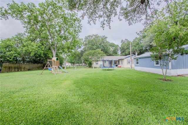 view of yard with a playground, fence, and a trampoline