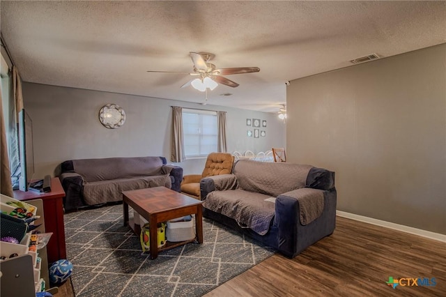 living room featuring a textured ceiling, a ceiling fan, baseboards, wood finished floors, and visible vents