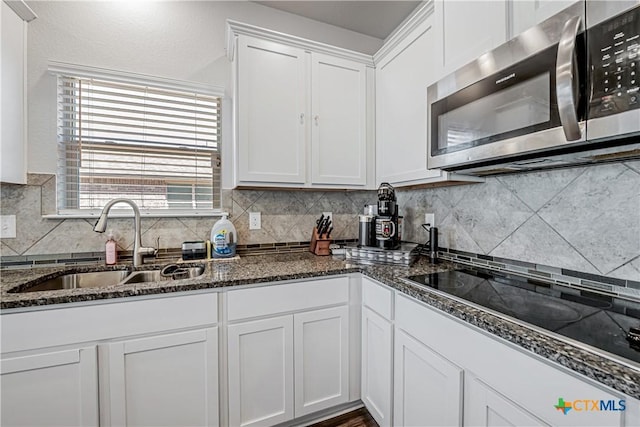 kitchen featuring stainless steel microwave, backsplash, black electric stovetop, white cabinets, and a sink