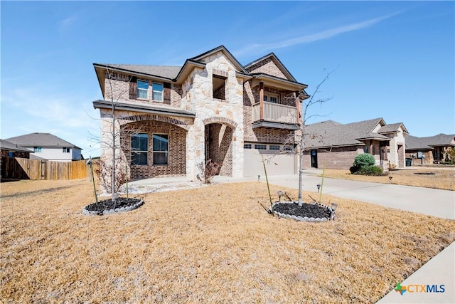 french provincial home featuring a balcony, fence, an attached garage, concrete driveway, and stone siding