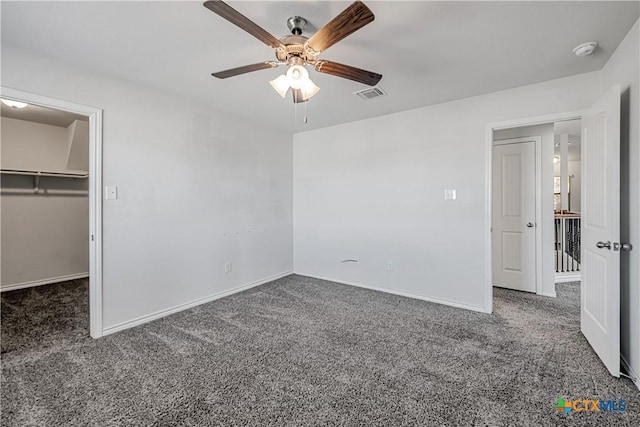 unfurnished bedroom featuring visible vents, a walk in closet, baseboards, carpet, and a ceiling fan