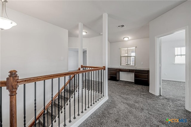 hallway with dark colored carpet, visible vents, an upstairs landing, and a healthy amount of sunlight