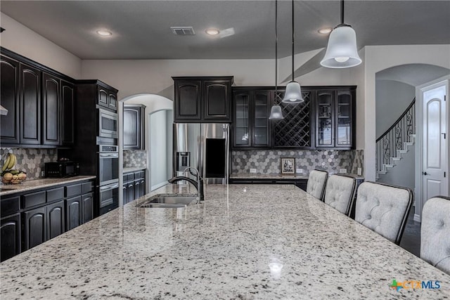 kitchen with light stone countertops, appliances with stainless steel finishes, tasteful backsplash, sink, and pendant lighting