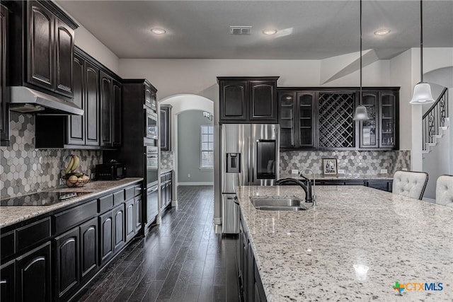 kitchen with hanging light fixtures, dark hardwood / wood-style floors, light stone countertops, appliances with stainless steel finishes, and tasteful backsplash