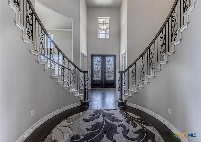 entrance foyer featuring french doors, a towering ceiling, ornamental molding, a notable chandelier, and dark hardwood / wood-style flooring