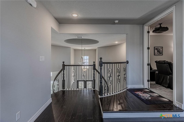 hall with a textured ceiling, hardwood / wood-style flooring, and an inviting chandelier