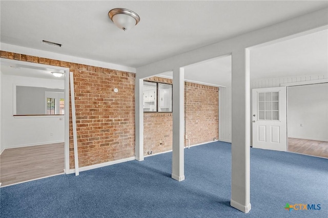 carpeted spare room featuring brick wall