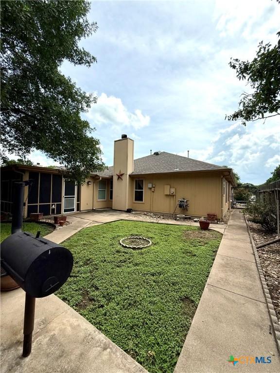 1828 Winchester Dr, Temple, TX 76502 - back of property with a sunroom, a patio area, a chimney, and a shingled roof