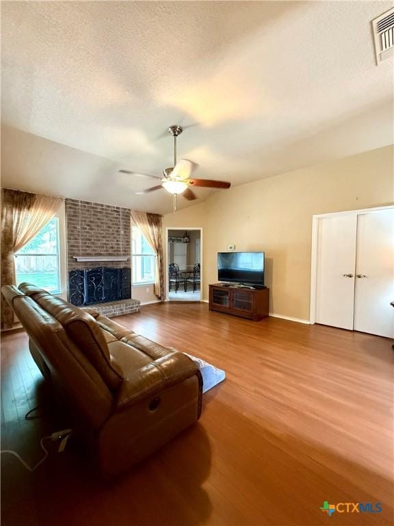 1828 Winchester Dr, Temple, TX 76502 - living room with wood finished floors, a ceiling fan, a brick fireplace, a textured ceiling, and vaulted ceiling