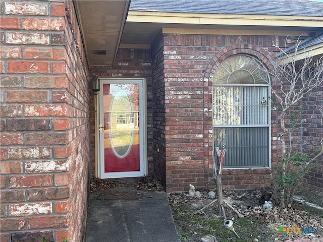 doorway to property with roof with shingles and brick siding