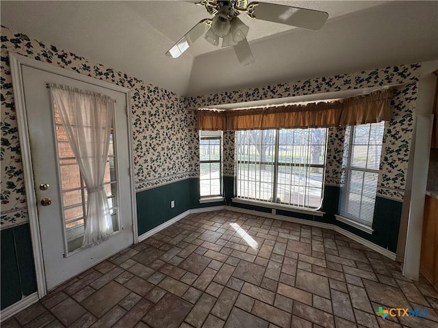 interior space with brick floor, a wainscoted wall, lofted ceiling, a ceiling fan, and wallpapered walls