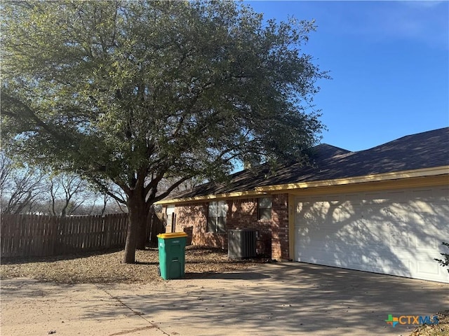 view of home's exterior with central air condition unit, a shingled roof, concrete driveway, an attached garage, and fence