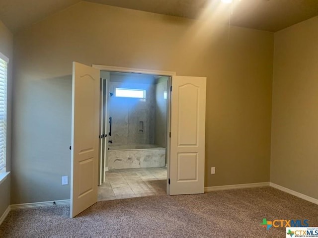 unfurnished bedroom featuring connected bathroom, light carpet, and lofted ceiling