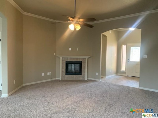 unfurnished living room with a tile fireplace, light carpet, ceiling fan, and ornamental molding