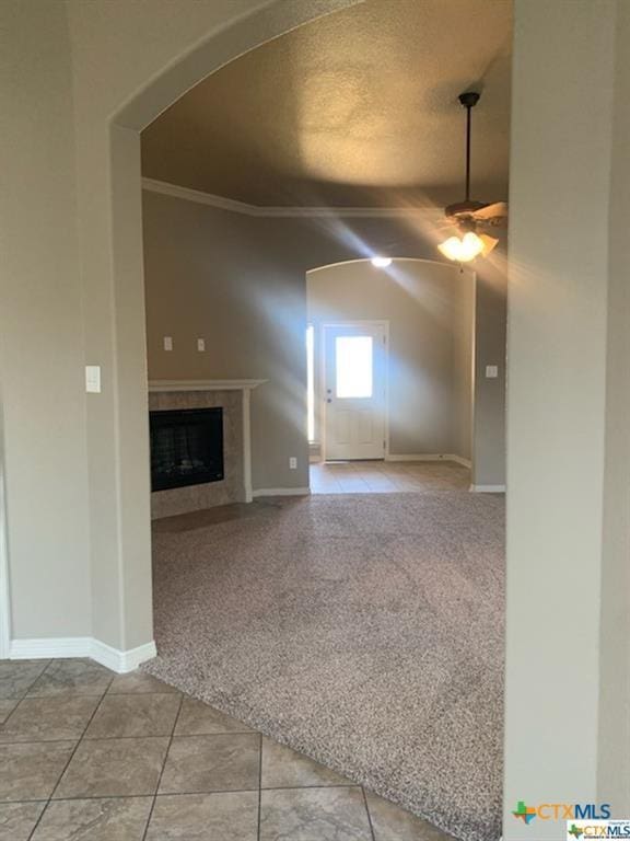 unfurnished living room with ceiling fan, light tile patterned flooring, a textured ceiling, and ornamental molding