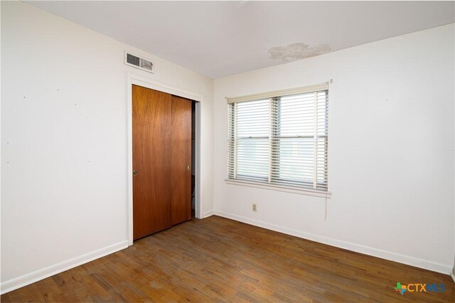 unfurnished bedroom with baseboards, a closet, wood finished floors, and visible vents