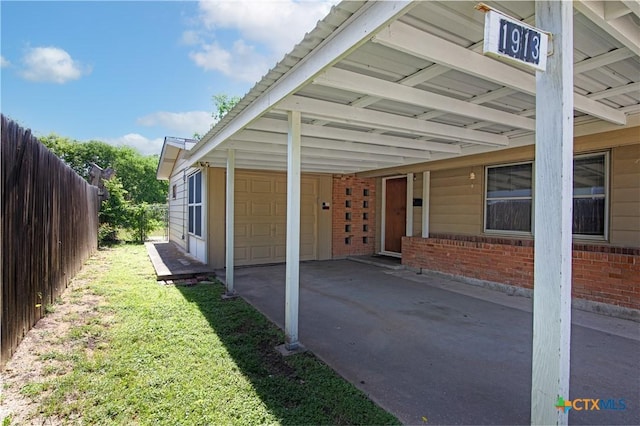 view of side of home with fence, brick siding, a garage, a carport, and driveway