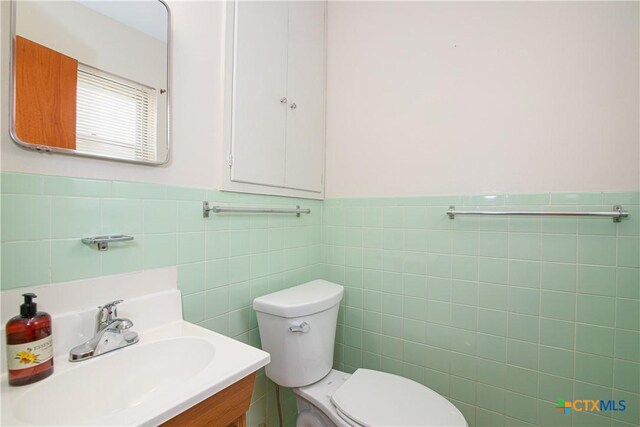 bathroom with toilet, tile walls, wainscoting, and vanity